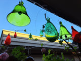 Colorful rinch green and leaf green and red glass bells and drops hanging from a roof with a clear blue sky in the background