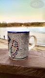 longdesc=" Large Mosaic Glazed Ceramic Mug that has two Red yellow Fishes and a blue and green basket containing round red and yellow pieces of bread loaves, which have been pattern pressed with a mosaic shape in black color. The almost square mosaic bord